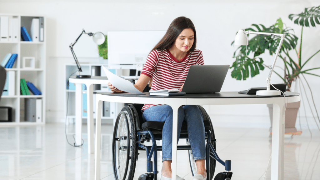 An image of a staff member in a wheel chair working in her office with her accessible desk.