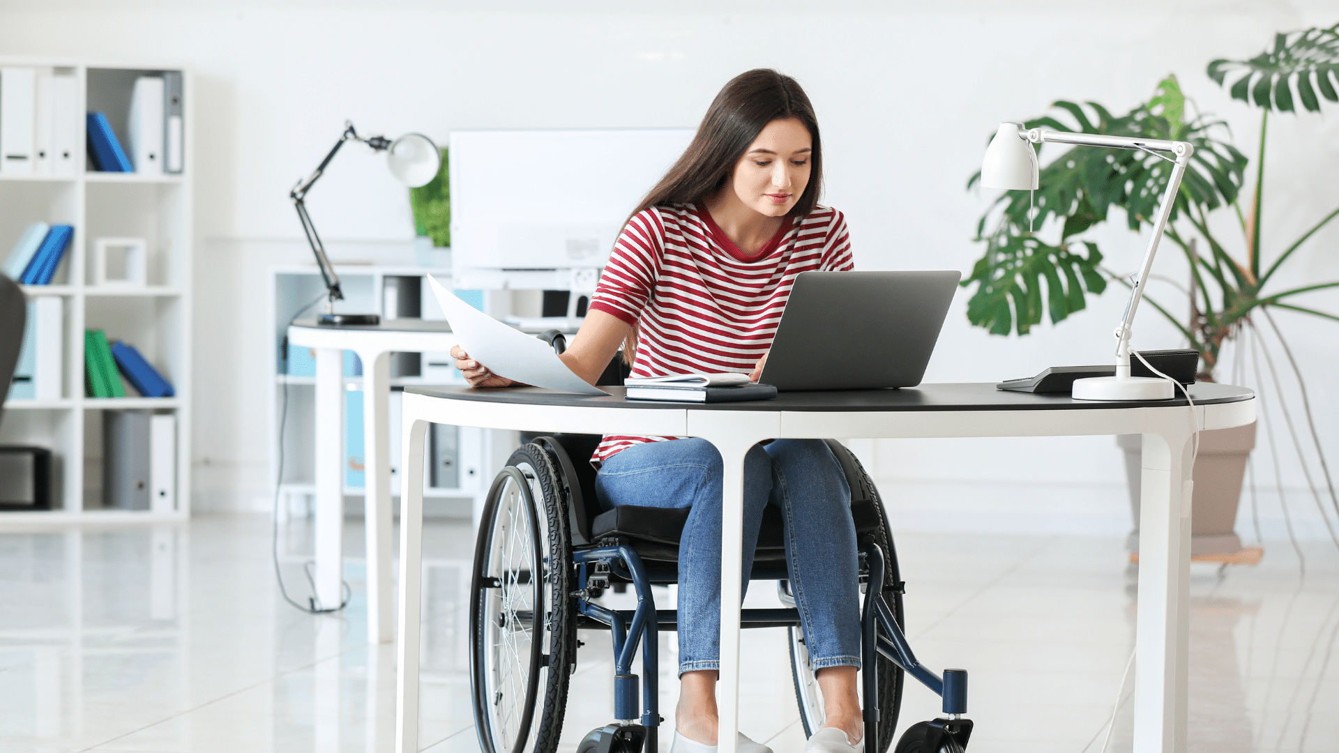 An image of a staff member in a wheel chair working in her office with her accessible desk.